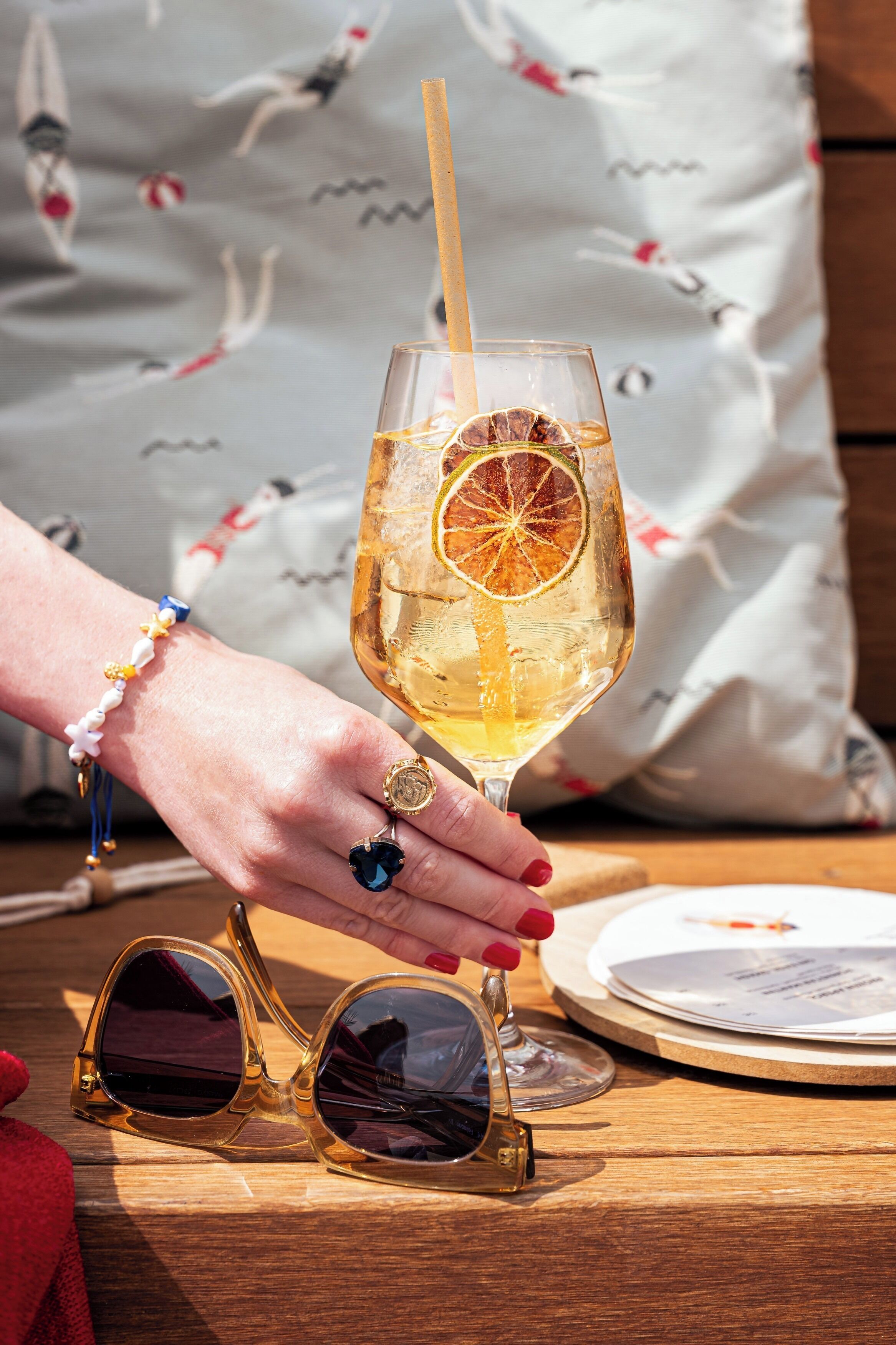 Eine Hand hält ein Glas mit Orangenscheibe, einem Holzhalm und einem goldenen Ring.