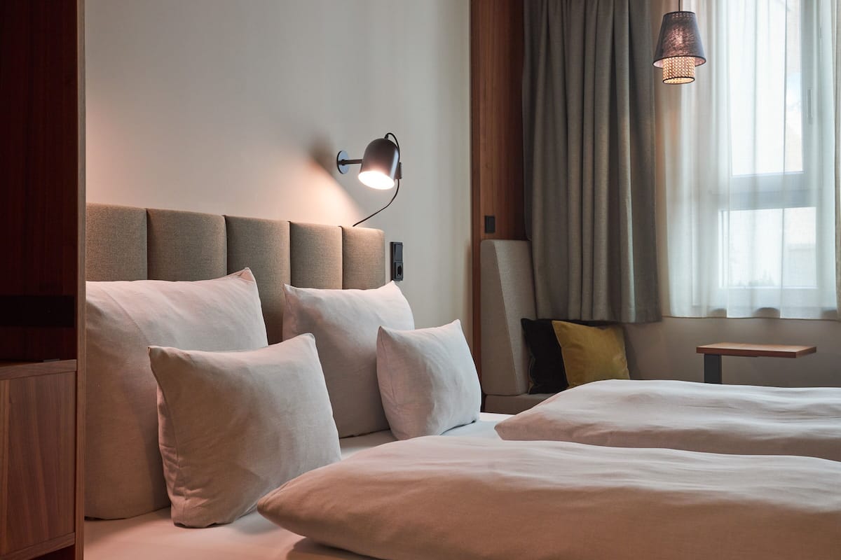A hotel room with a large bed, a bedside table, a lamp, and a window with curtains.