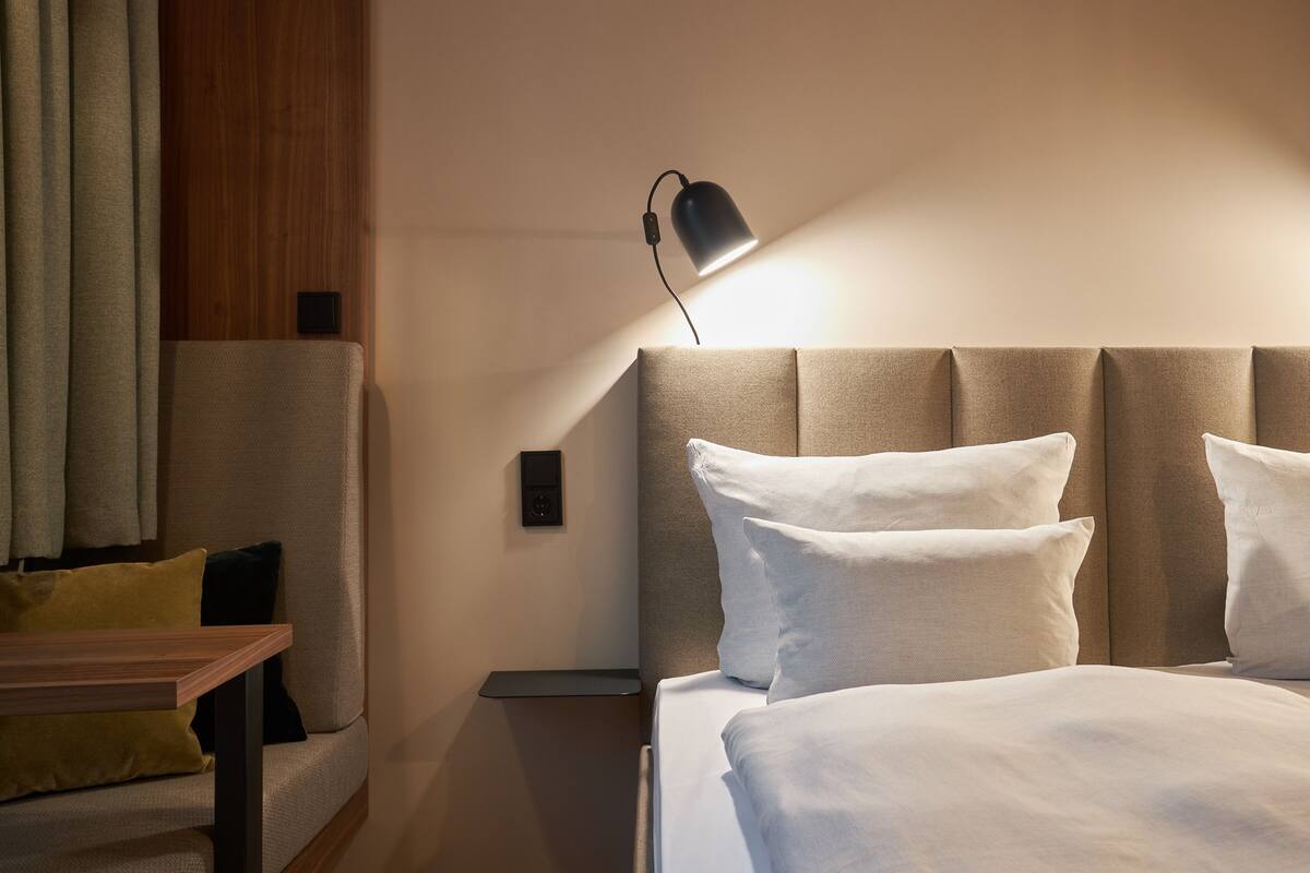 A hotel room with a bed, bedside table, lamp, and a sofa with cushions.