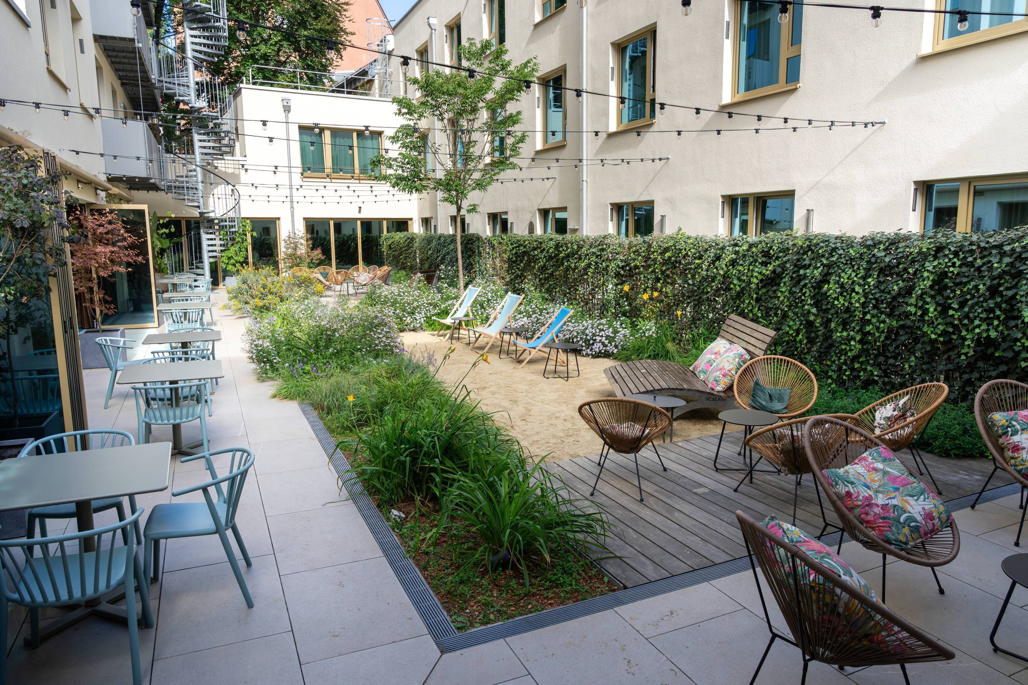 A courtyard with outdoor seating, a small tree, and a hedge.