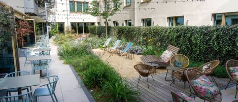A courtyard with outdoor seating, a small tree, and a hedge.