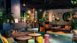 A modern lounge area with a fireplace, round tables, colorful stools, and various plants. - Cocoon München Sendlinger Tor (Munich)