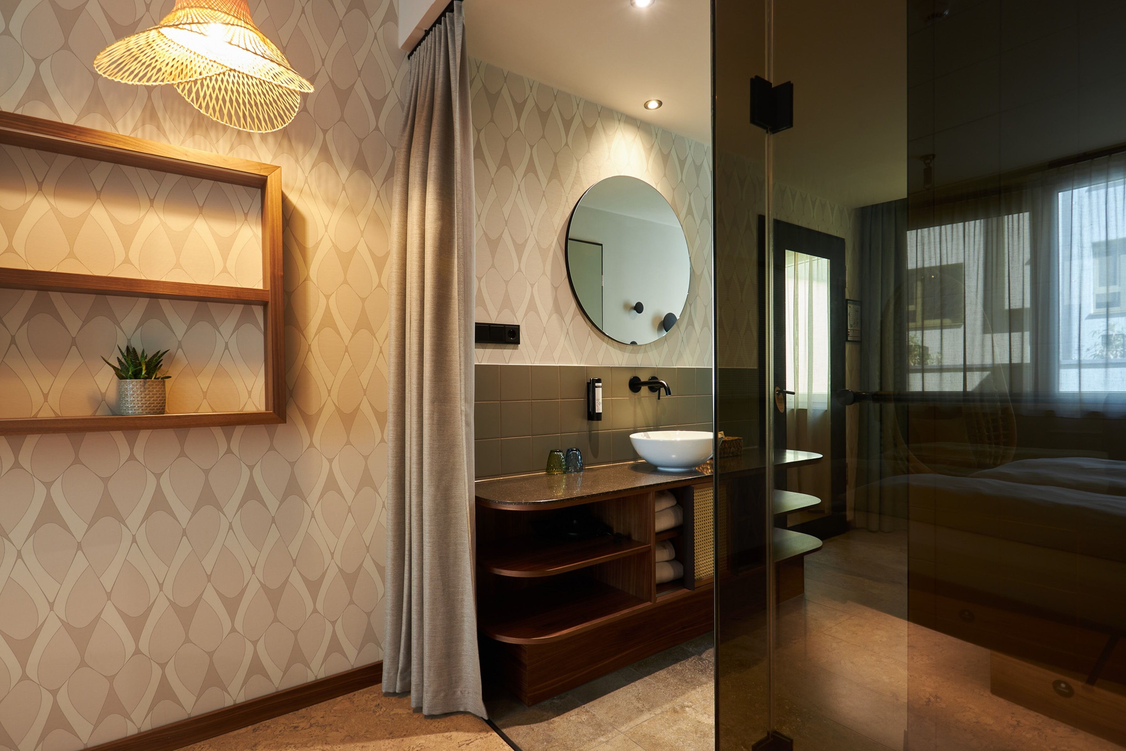 Une salle de bain moderne avec un miroir rond, un lavabo et une étagère ornée d’une plante.
