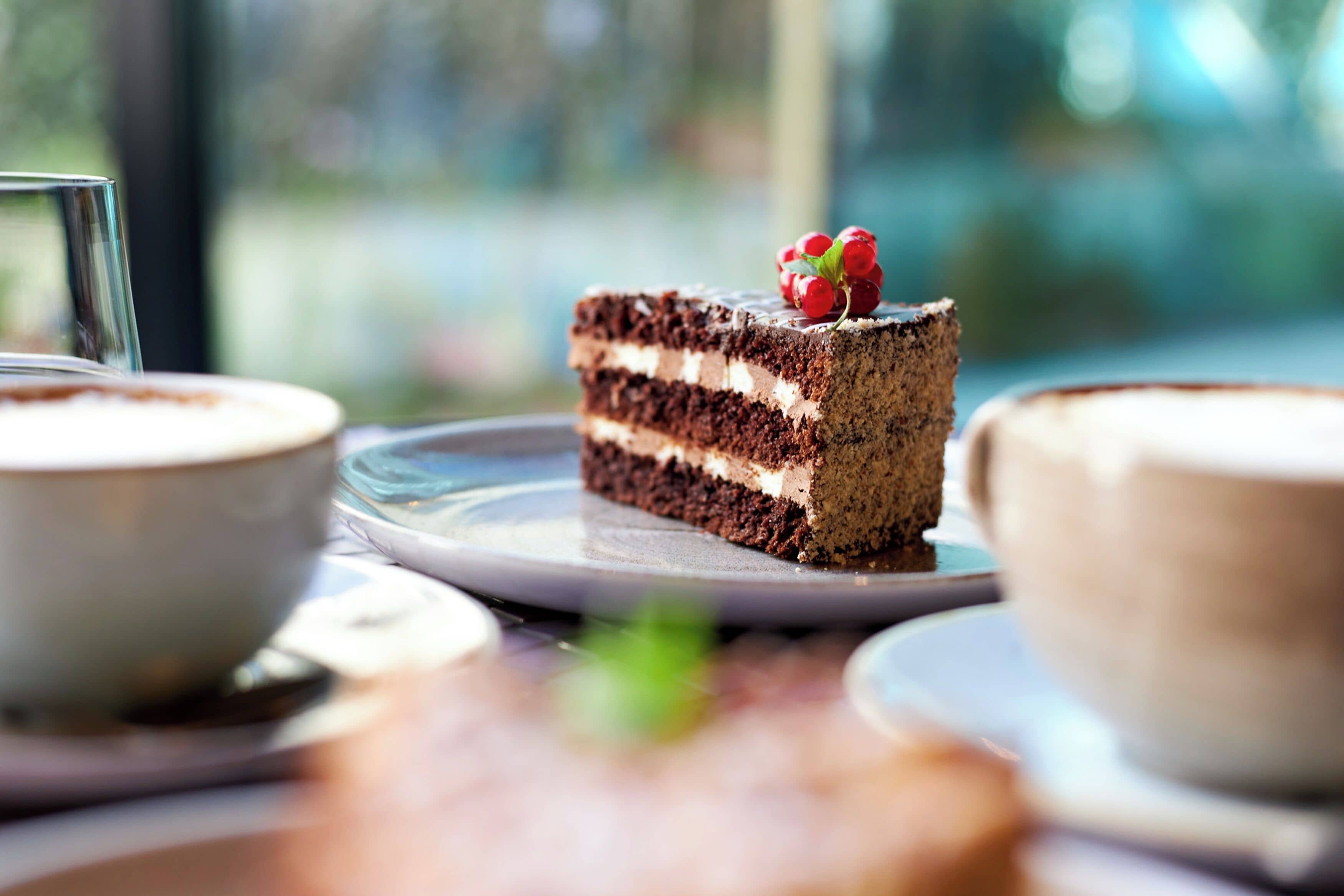 Une part de gâteau au chocolat à plusieurs couches, surmontée d’une cerise, servie sur une assiette blanche.