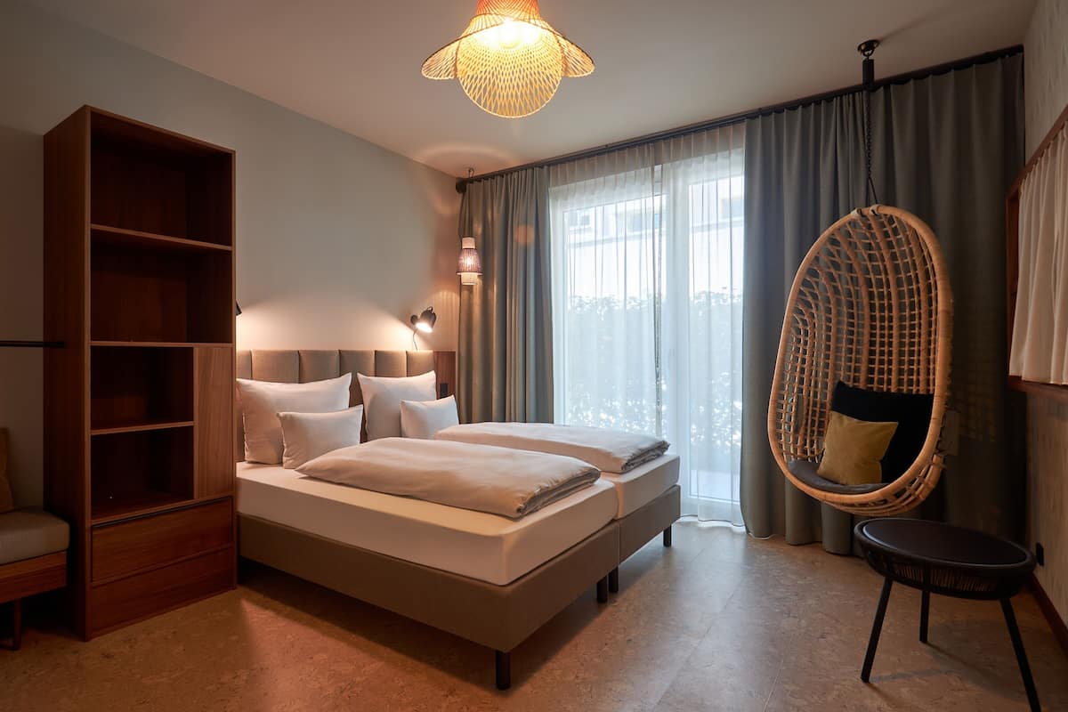 A bedroom with a large bed, a wooden wardrobe, a hanging chair, and a large window with curtains.