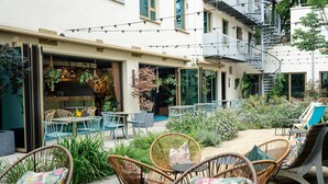 An outdoor seating area with wicker chairs and tables, surrounded by greenery and plants. - Cocoon München Sendlinger Tor (Munich)