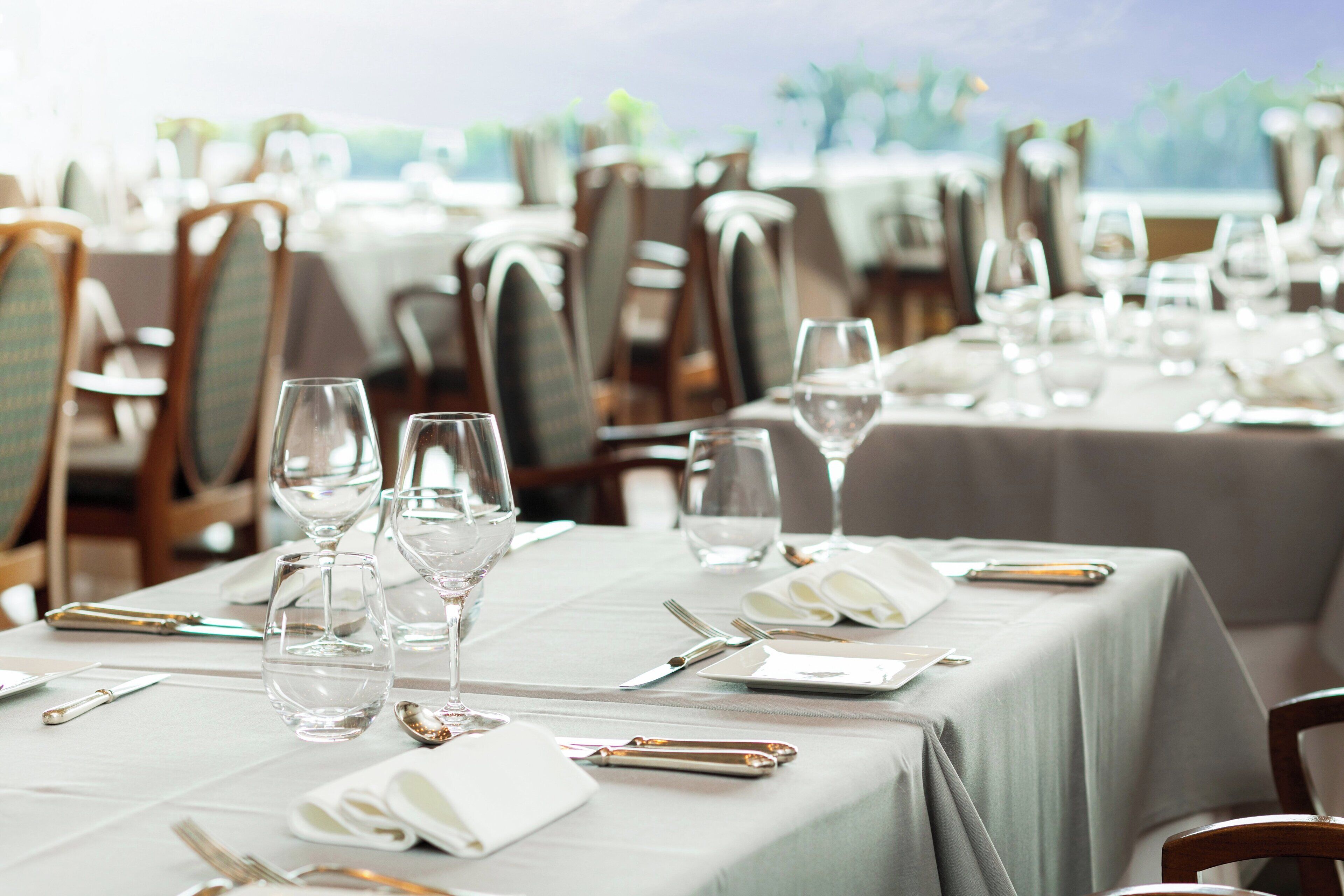 A dining area with tables set for service, featuring chairs, cutlery, and glassware.
