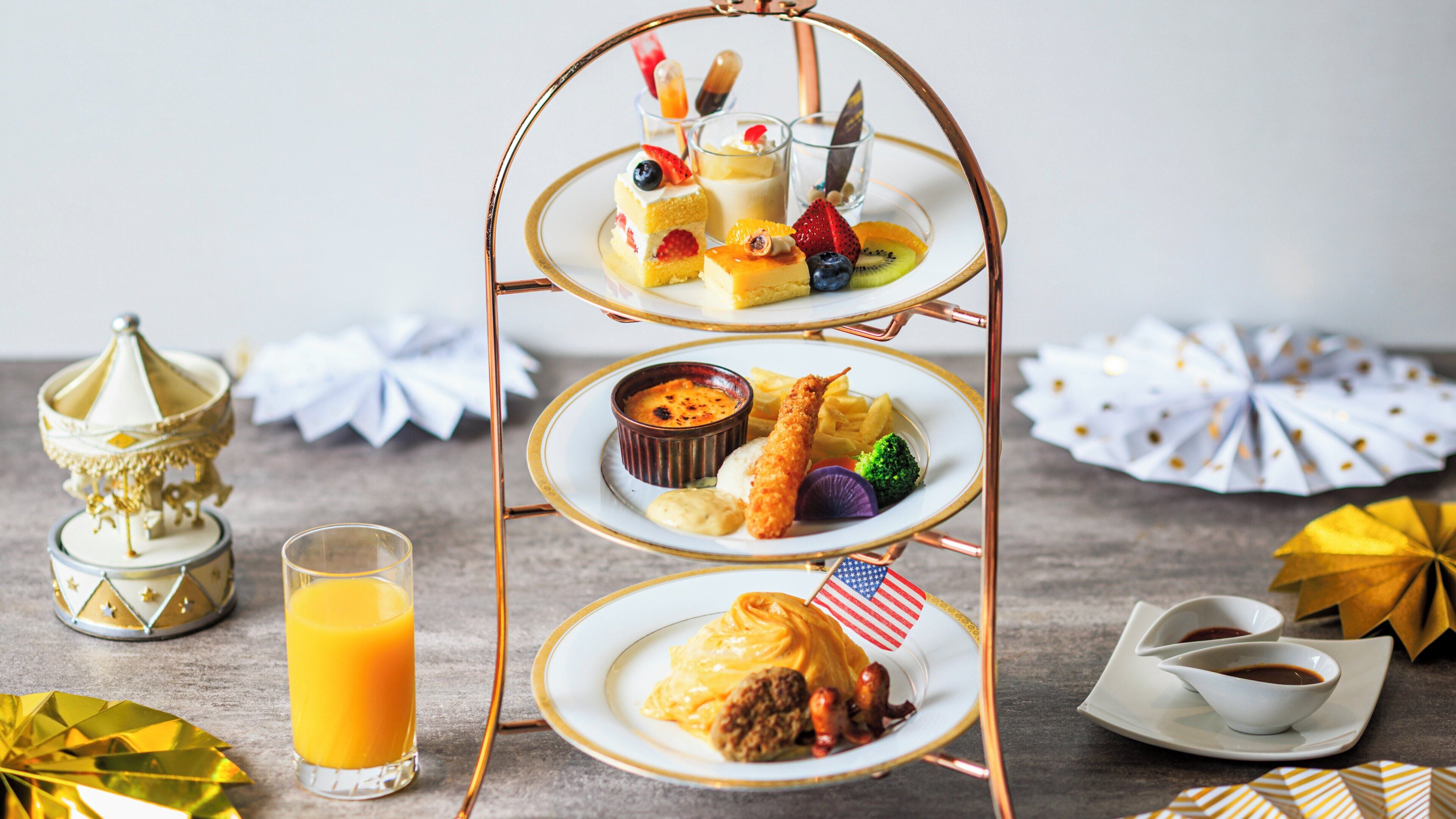 Ein mehrstöckiges Serviertablett mit verschiedenen Desserts und einem Glas Orangensaft.