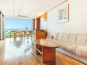 A modern living room with a wooden floor, a beige sofa, a wooden coffee table, and a dining area with chairs and a table.