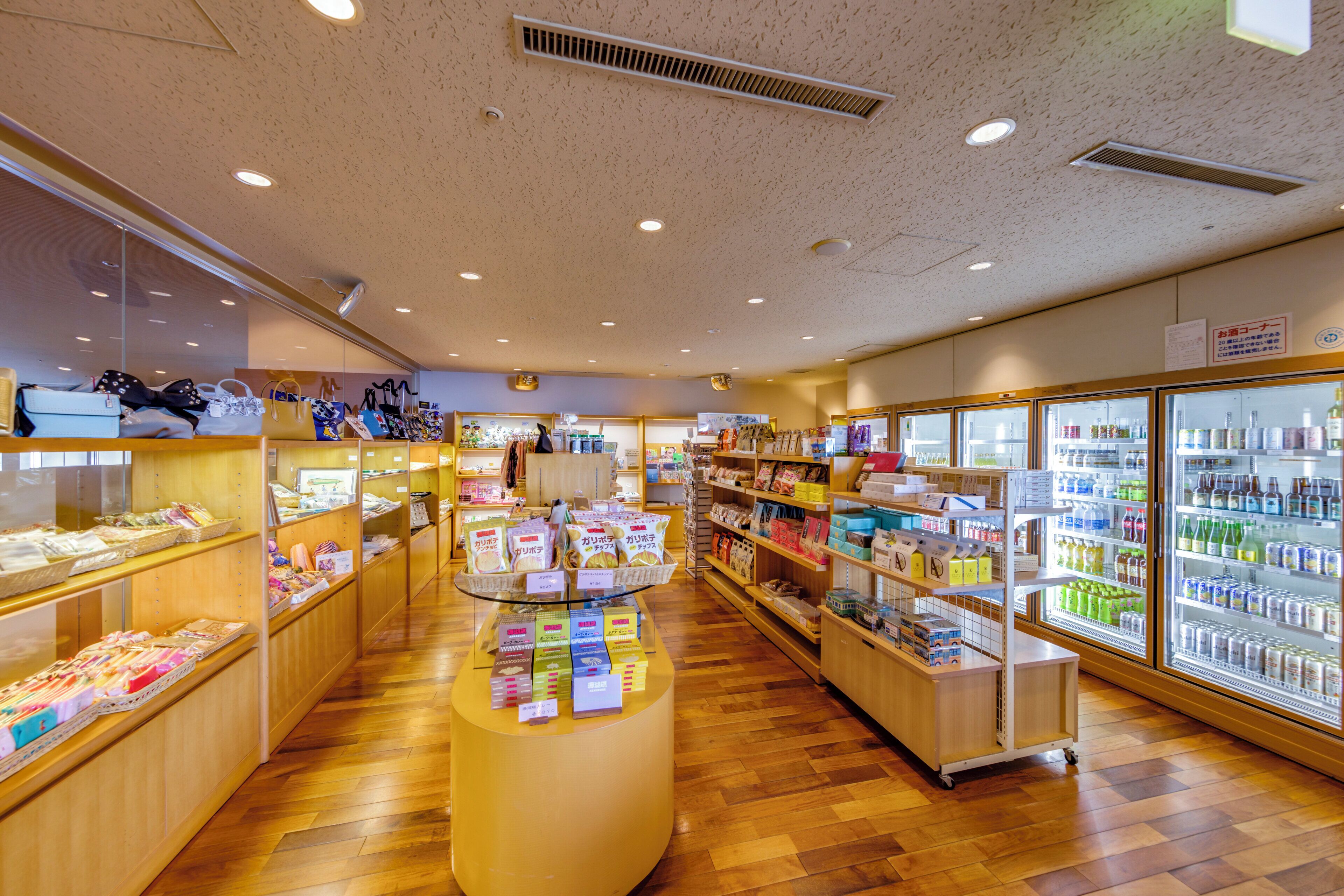 A well-lit store with wooden flooring, shelves stocked with various products, and a refrigerated section on the right.
