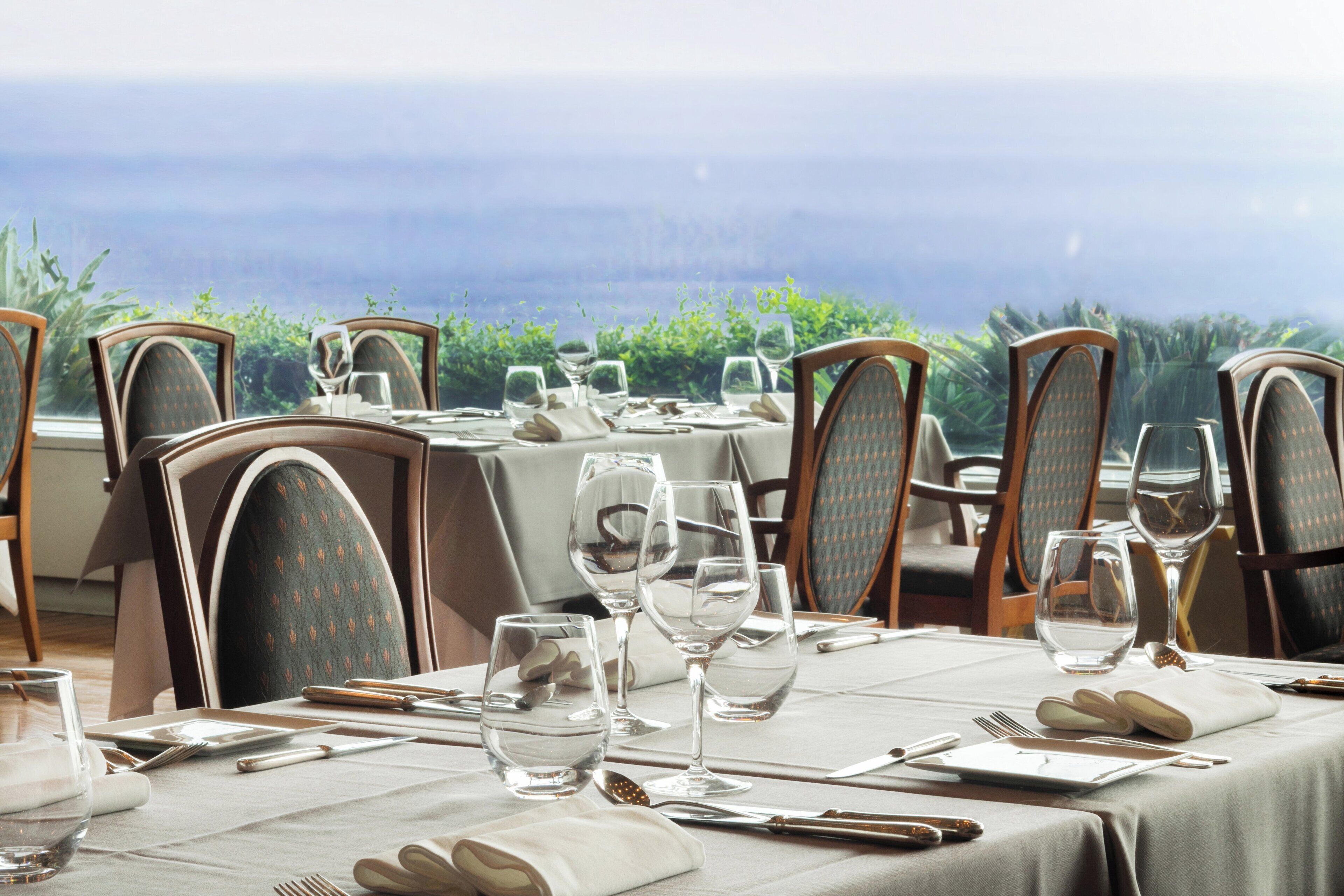 A table set for dining with chairs, a view of the ocean, and a tablecloth.