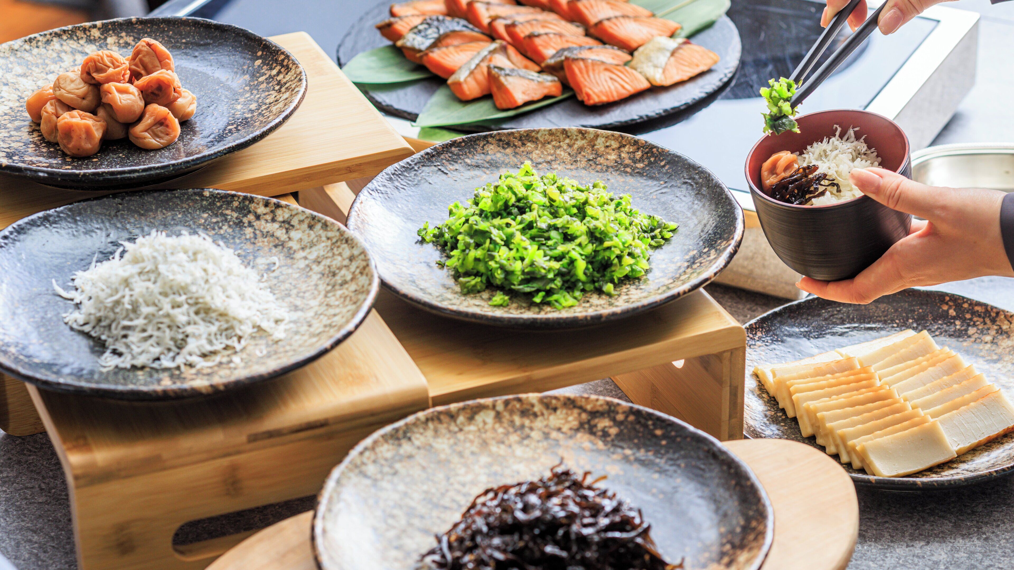 A variety of dishes on a table, including rice, green vegetables, and fish.