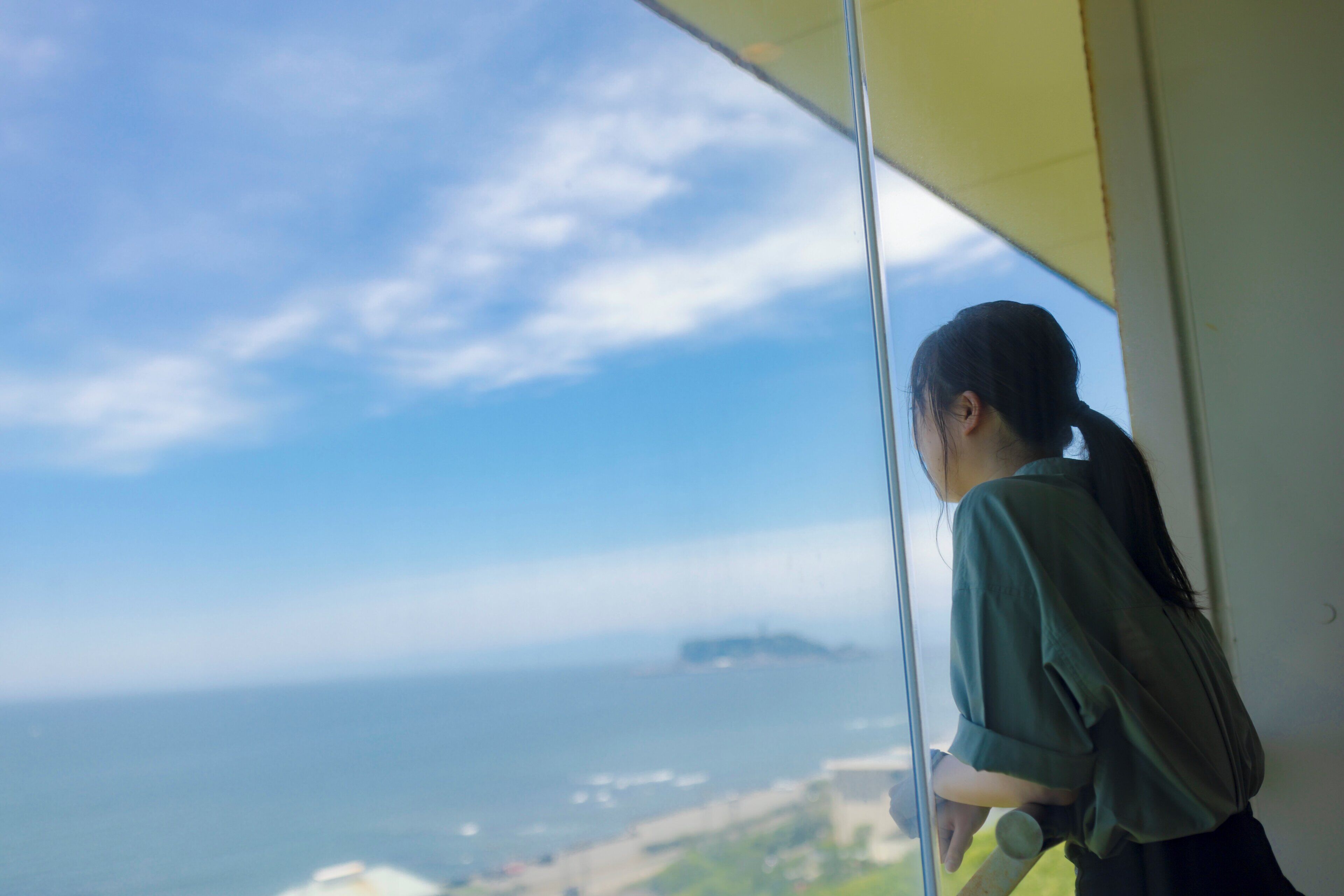 A person leaning on a window with a view of the ocean and distant land.