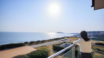 A balcony with a view of the sea, a paved area, and a distant town.