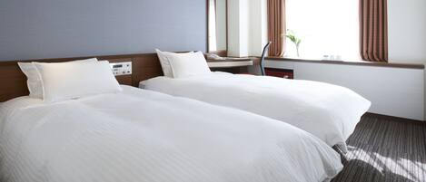 A hotel room with two beds, a desk, a chair, a window with curtains, and a plant.