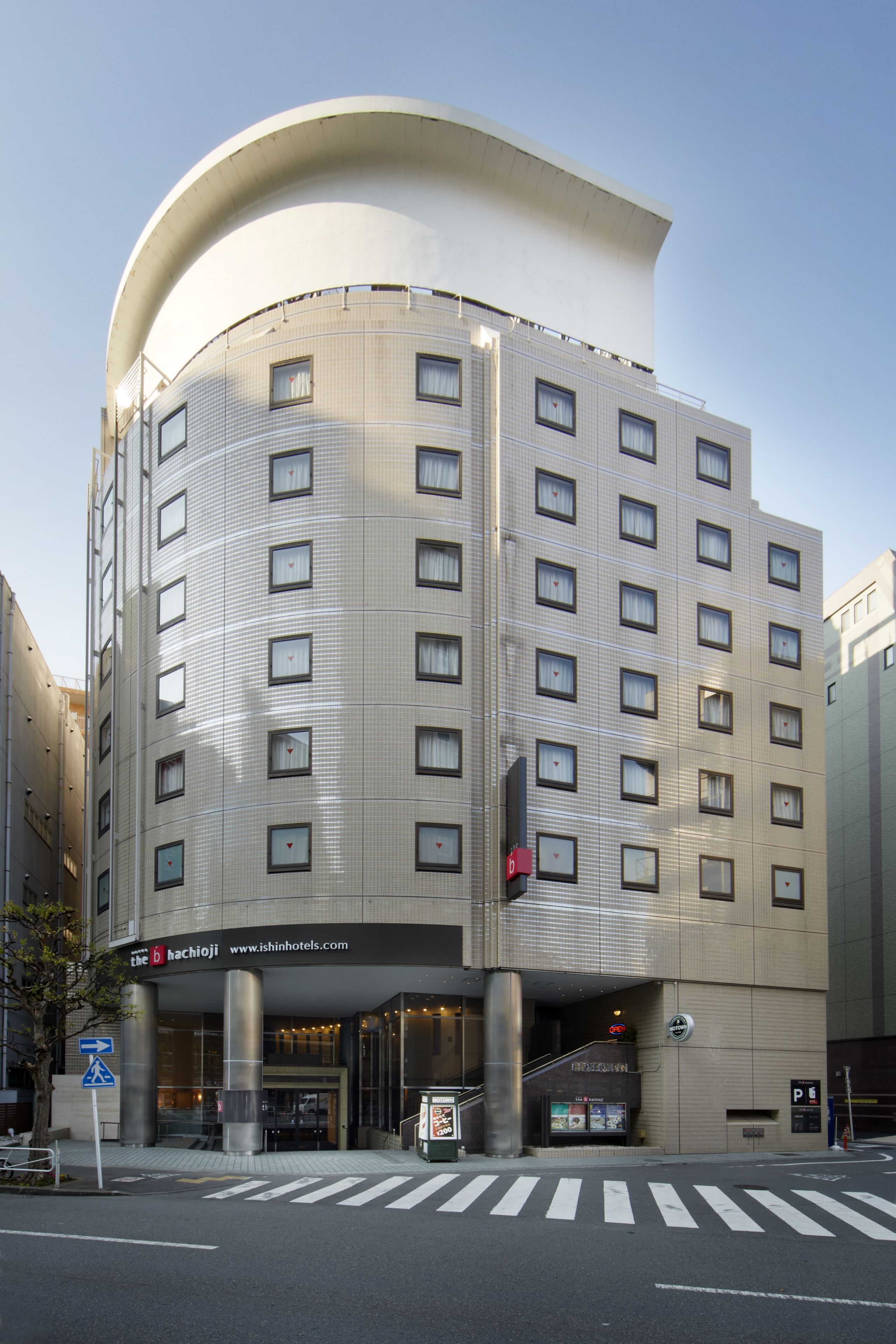 A modern hotel with a curved facade, multiple floors, and a visible entrance with a sign.