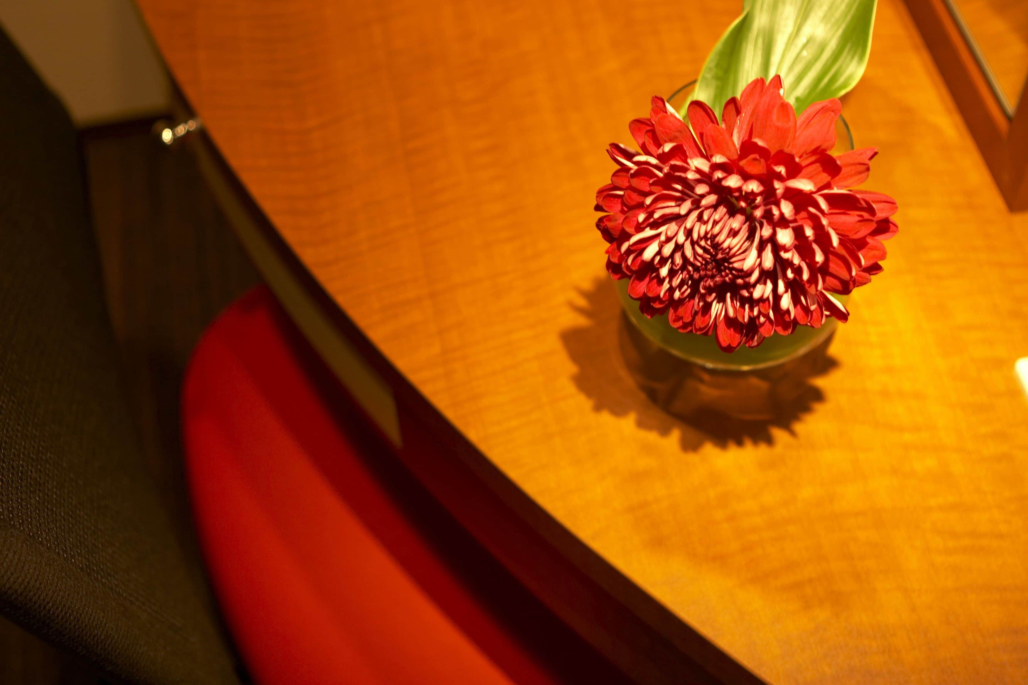 A wooden table with a red flower arrangement.
