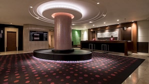 A hotel lobby with a central column, a reception desk, and a patterned carpet. - the b hachioji (Hachioji)