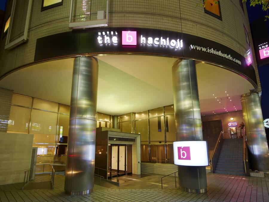Entrada de hotel com um letreiro 'b' em destaque, escadas e fachada de vidro.