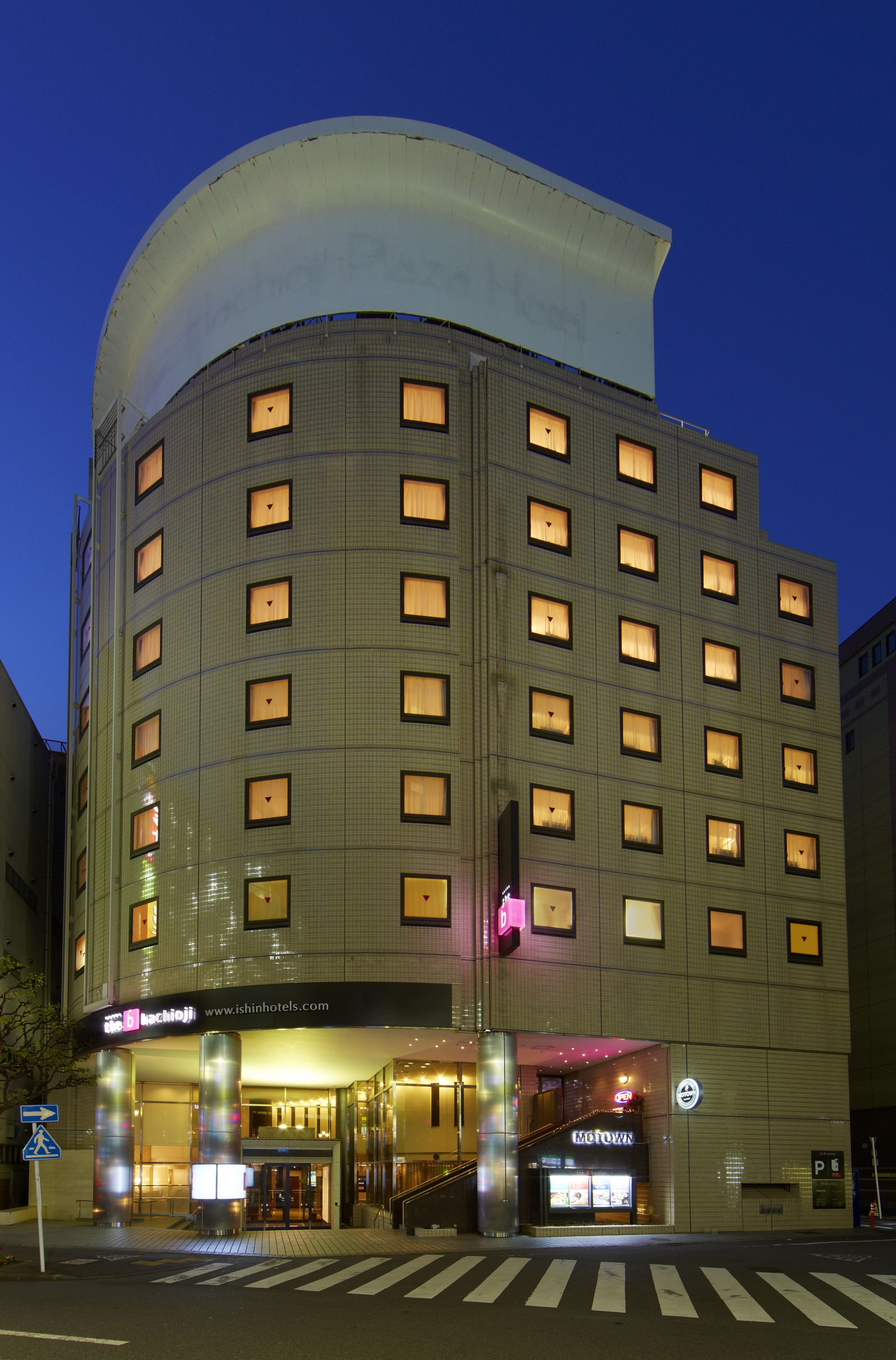 A multi-story hotel with a curved facade, illuminated windows, and a visible entrance with a staircase.