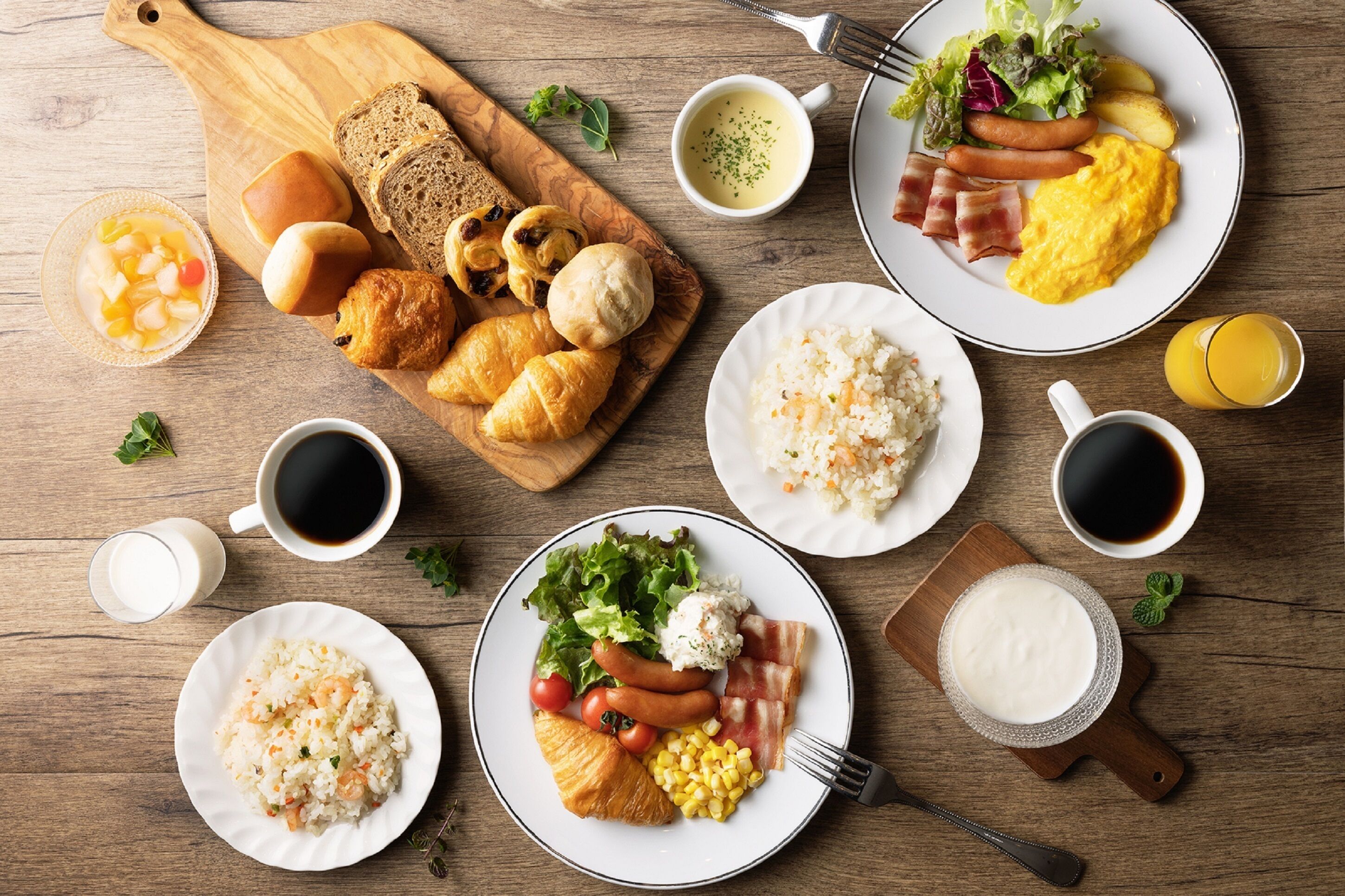 A breakfast spread with croissants, sausages, bacon, eggs, and various fruits and vegetables on wooden tables.