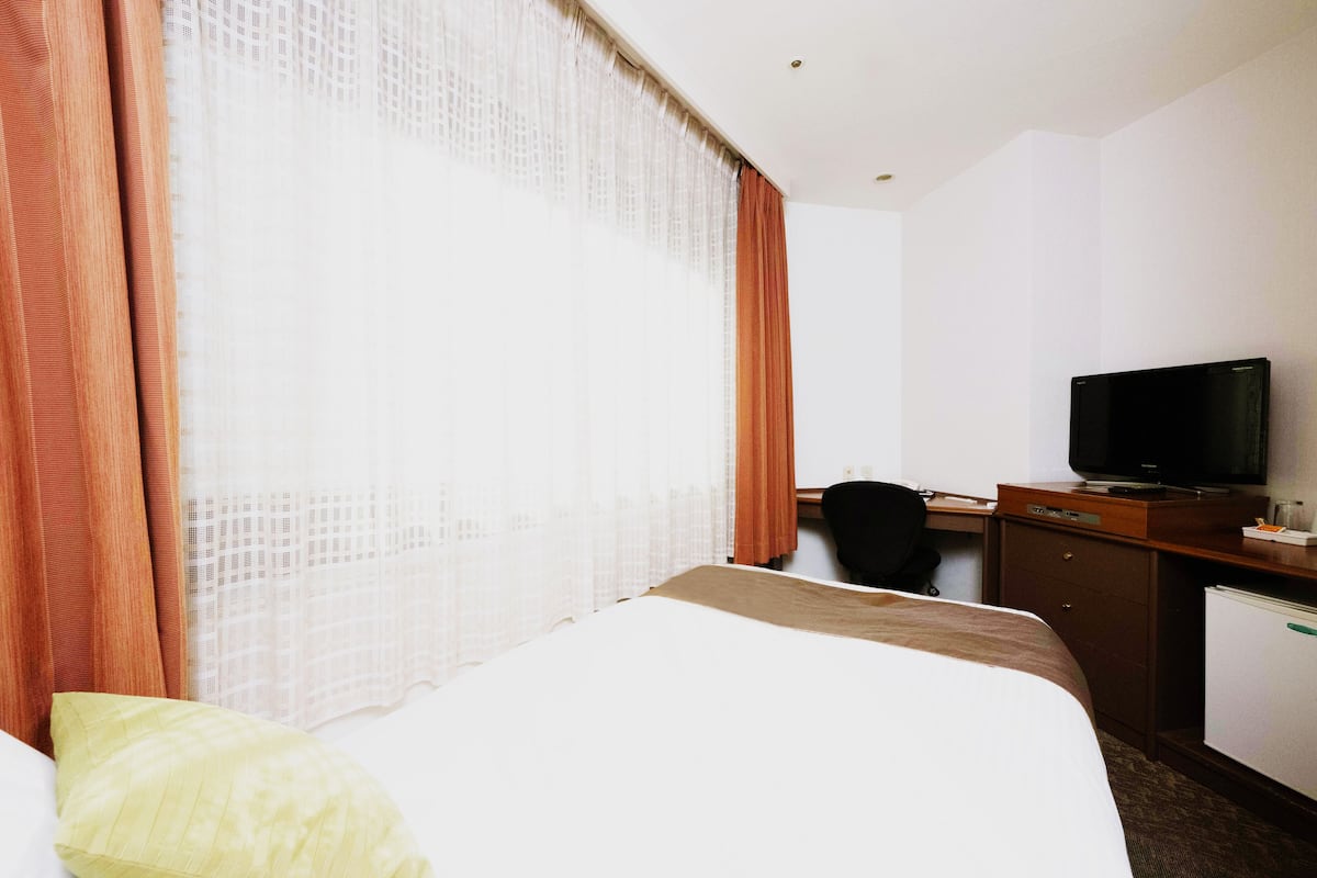 Una habitación de hotel con cama, escritorio, silla, televisor y un refrigerador pequeño.