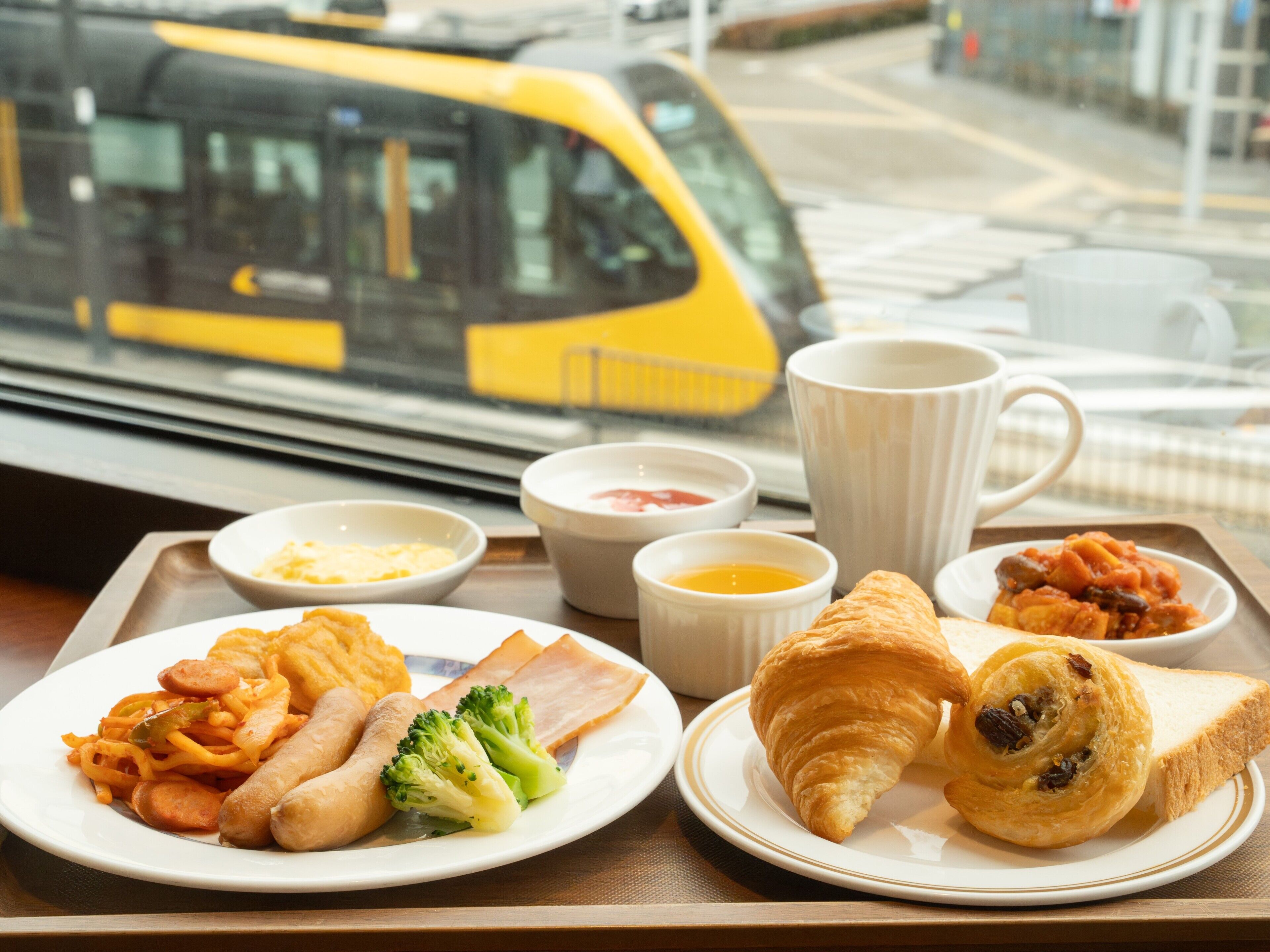 A tray with breakfast items including sausages, scrambled eggs, toast, and croissants.