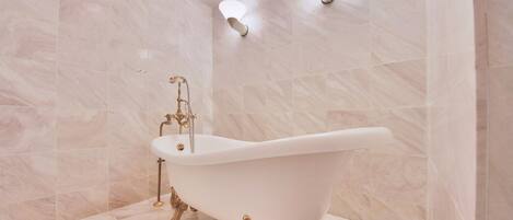 Una bañera independiente en un baño con azulejos de mármol e iluminación empotrada.
