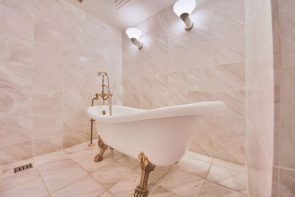 Una bañera independiente en un baño con azulejos de mármol e iluminación empotrada.