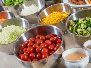 Une table de buffet proposant divers plats, notamment des tomates, du maïs, des brocolis et des légumes coupés en julienne.