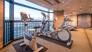 Une salle de sport équipée de matériel d’exercice, dotée de grandes fenêtres et offrant une vue sur le paysage urbain.