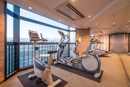 A gym with exercise equipment, large windows, and a view of a cityscape.