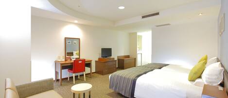A hotel room with a bed, a desk, a chair, and a small table.