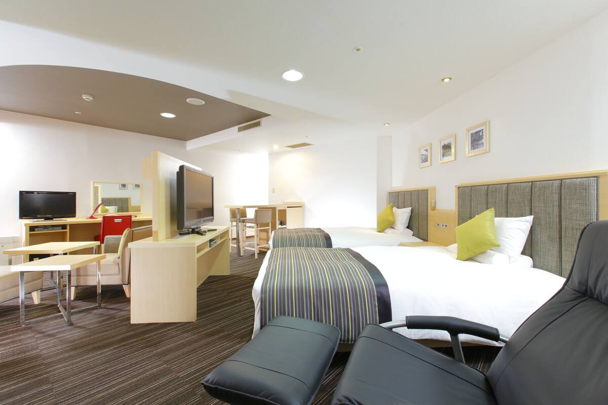 Habitación de hotel con cama, dos mesitas de noche, escritorio con silla, televisor y sofá.