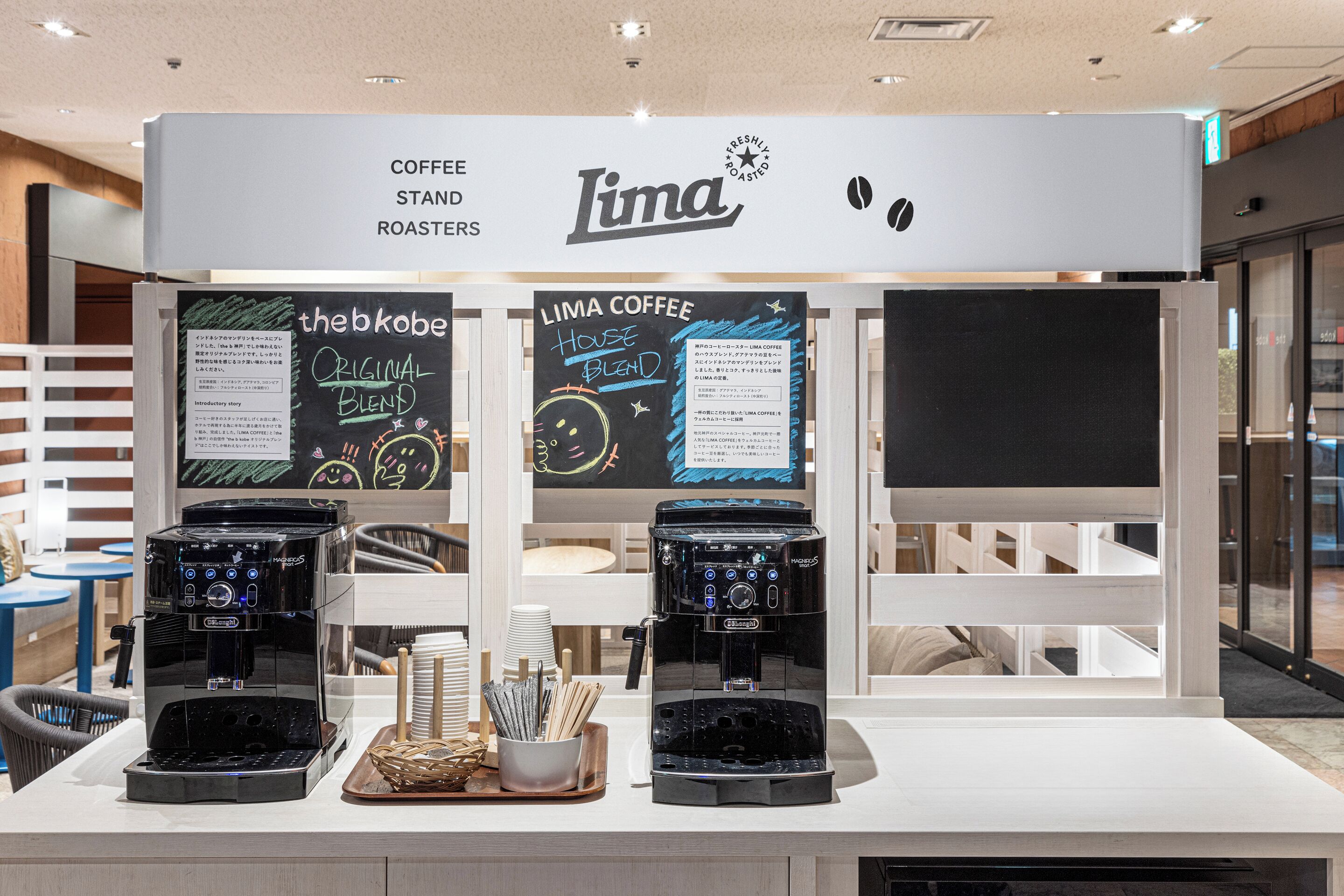 A coffee stand with two espresso machines, a menu board, and a sign that reads 'Lima Coffee Stand Roasters'.