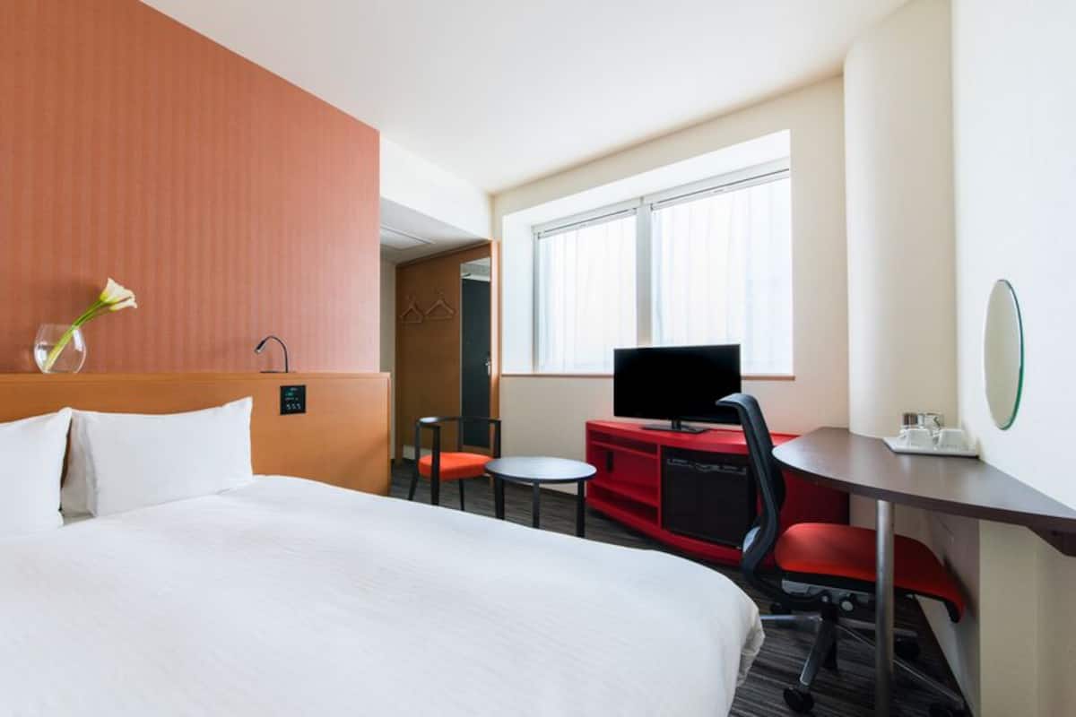 A hotel room with a large bed, a desk with a chair, a television, and a window.