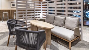 A modern lounge area with a sofa, two chairs, a small table, and a partition with a view of an escalator. - the b kobe (Kobe)