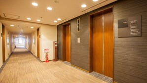 A hotel corridor with wooden doors, a fire extinguisher, and a sign listing guest rooms and amenities. - the b kobe (Kobe)
