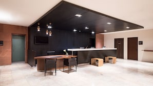 A modern reception area with a wooden reception desk, a flat-screen TV, and a seating area with chairs and stools. - the b kobe (Kobe)