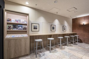 Un área de recepción con un mueble de madera que exhibe folletos, cuadros en la pared y una fila de taburetes de bar.