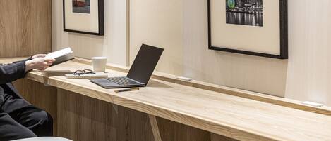 Un bureau en bois avec un ordinateur portable, un carnet et un stylo. Des photos encadrées sont accrochées au mur.