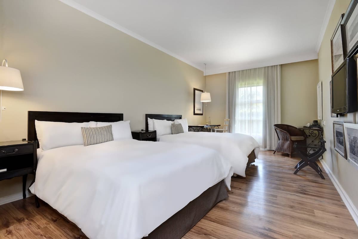 A hotel room with two beds, a desk, and a chair.