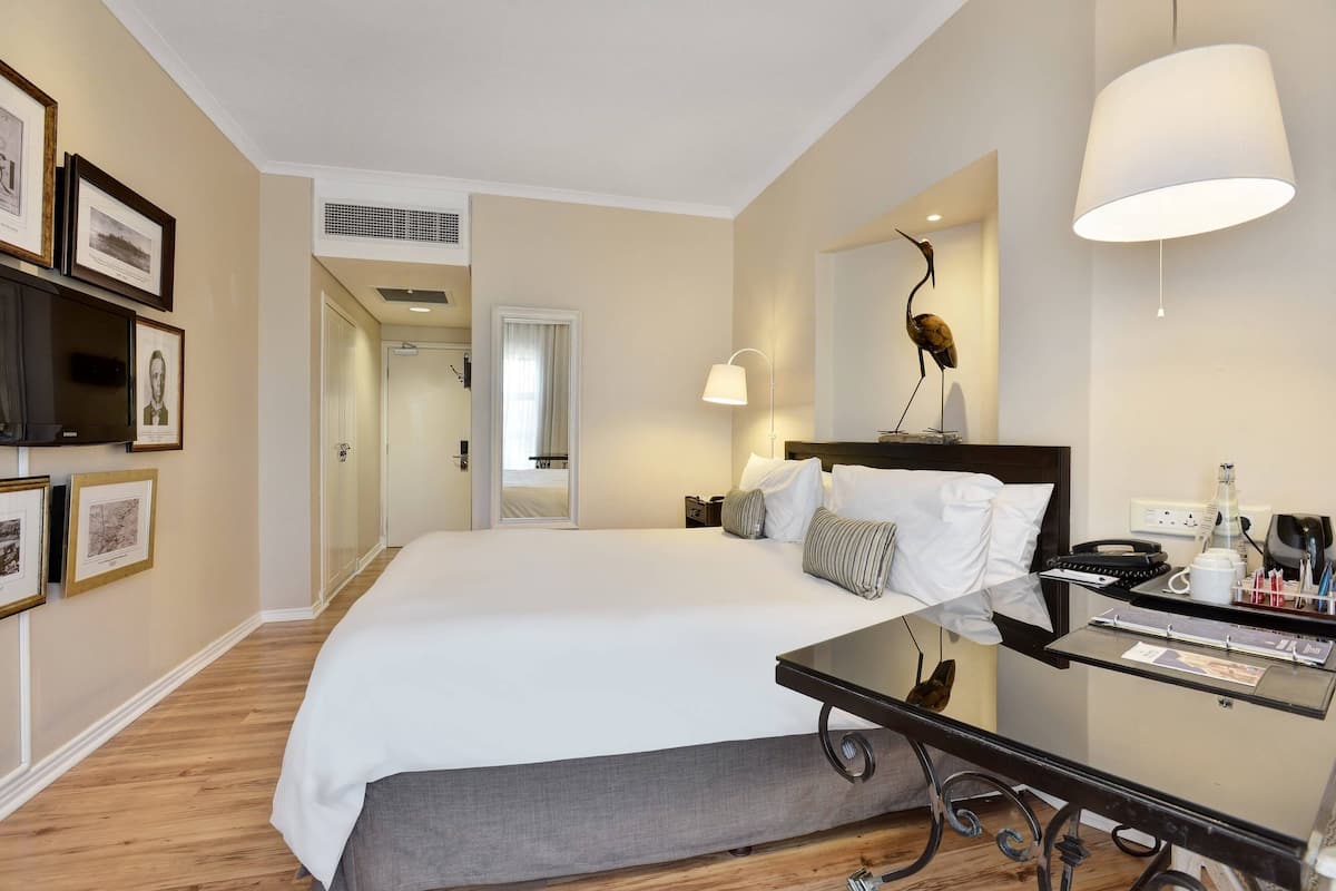 A hotel room with a large bed, bedside table, lamp, and framed pictures on the wall.
