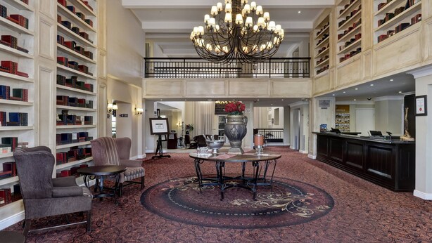A spacious lobby with a grand chandelier, a central round table, and extensive book-lined walls.
