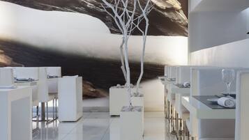 Un moderno hall de hotel con diseño minimalista, que presenta mobiliario blanco, un gran mural abstracto en la pared y una escultura de árbol blanco en el centro.