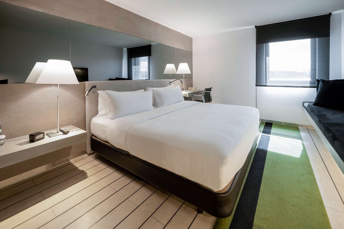 Una habitación de hotel moderna con una cama grande, lámparas de noche, un escritorio y vistas a la ciudad desde la ventana.