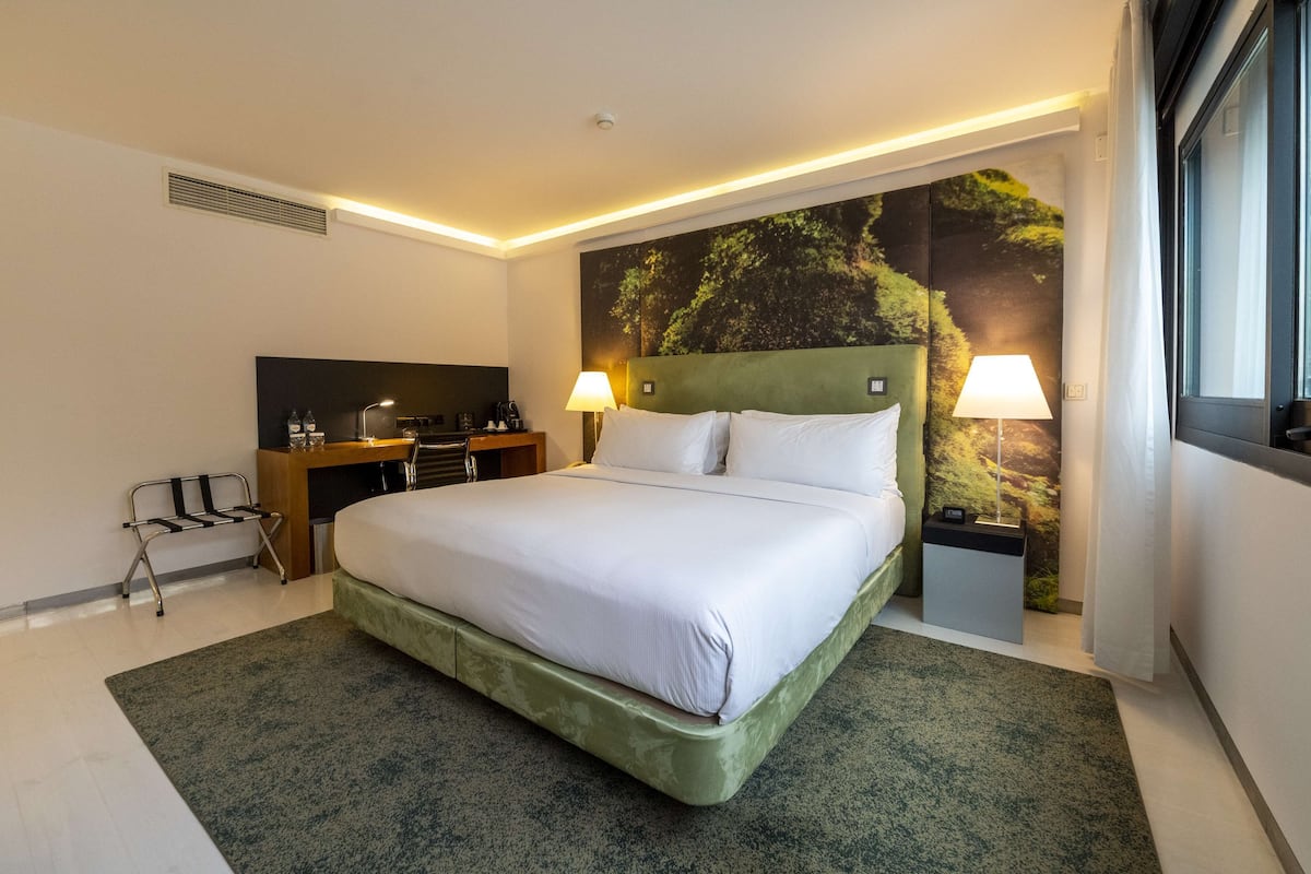 Habitación de hotel moderna con una cama grande, un escritorio, dos lámparas y un mural en la pared.