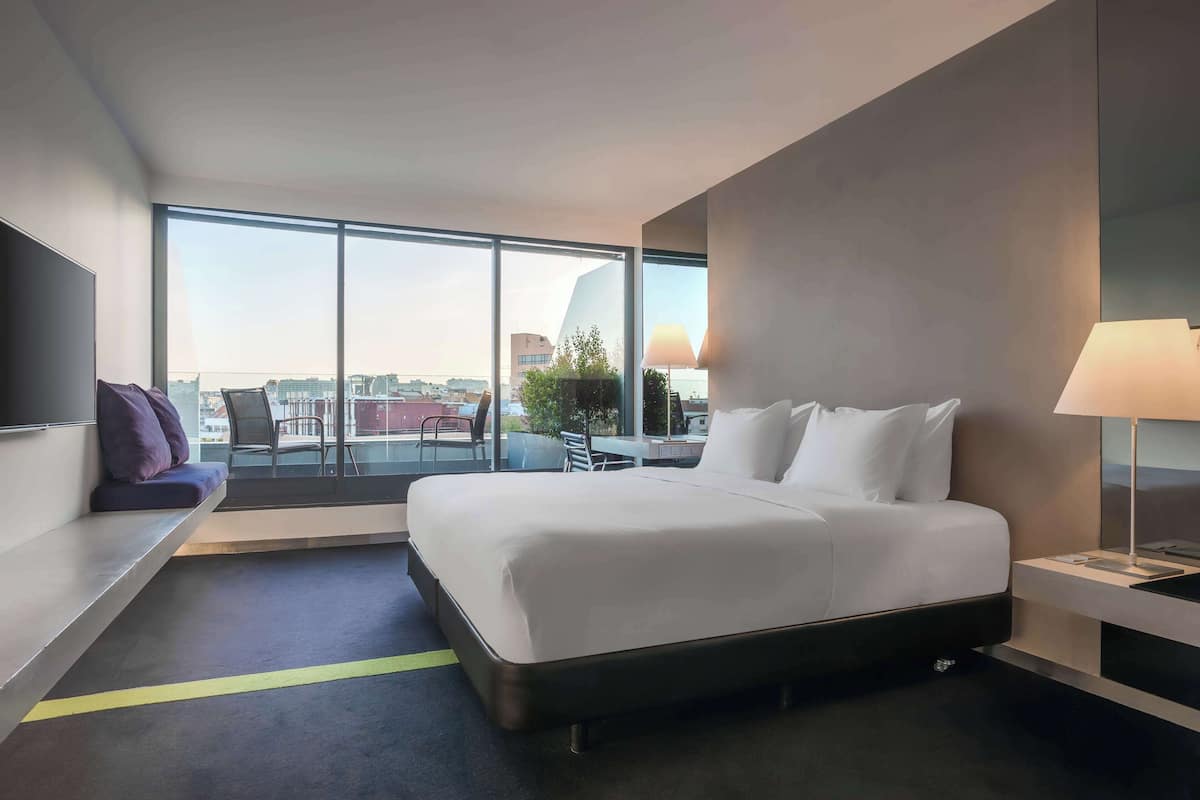 Una habitación de hotel moderna con una cama grande, un espacio de descanso con vistas y una mesa de comedor.