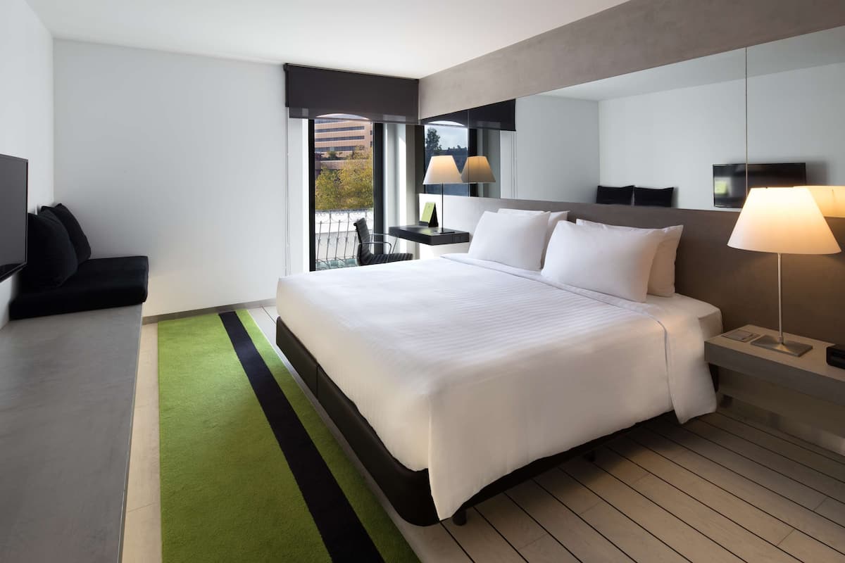 Una habitación de hotel moderna con una cama grande, una zona de estar con sofá, una mesita y un televisor.