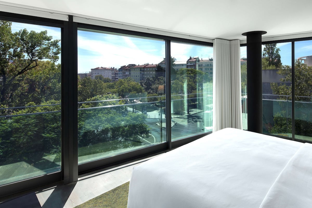 Habitación de hotel con ventanas amplias, una cama y vistas a un paisaje urbano.